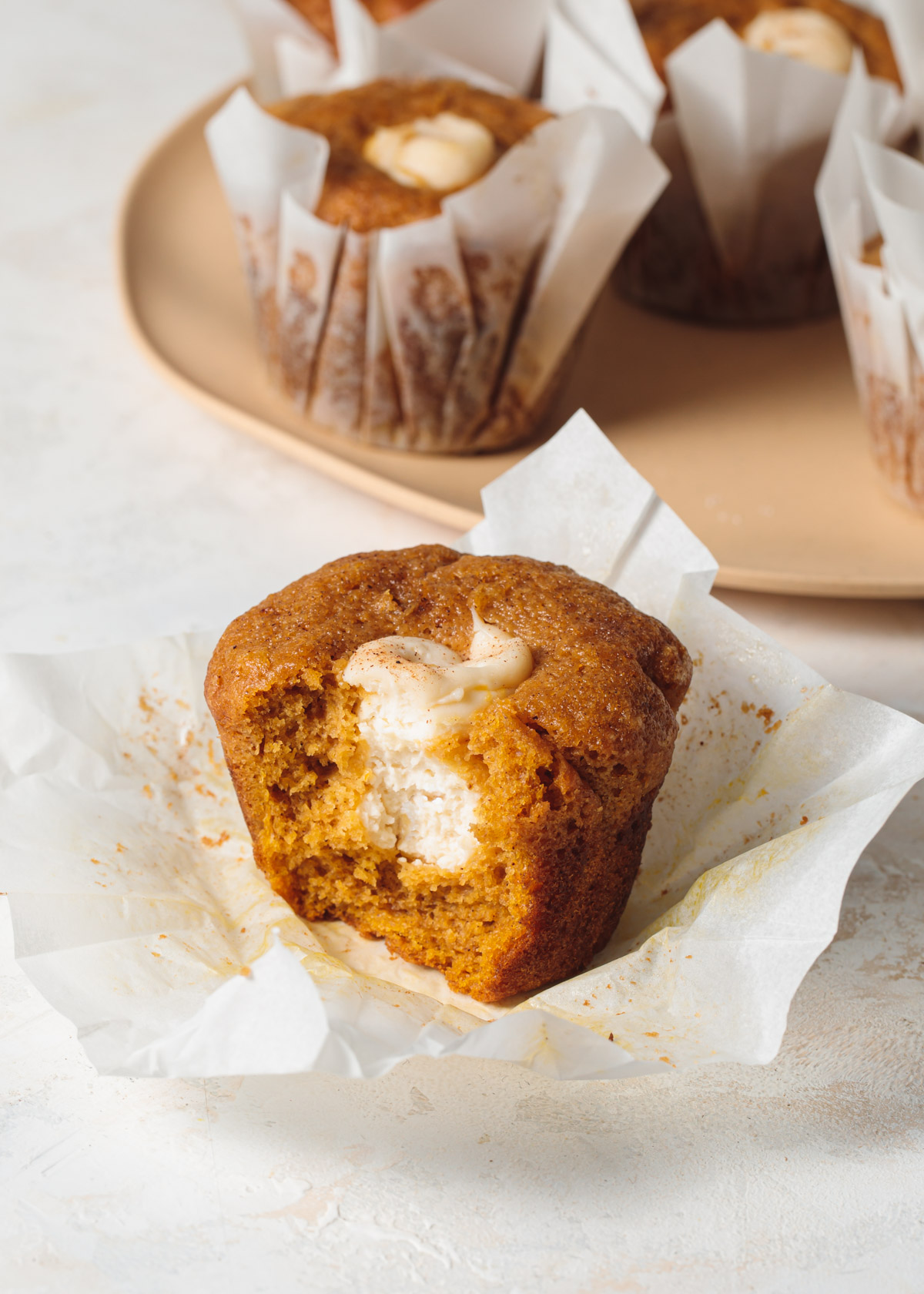 A pumpkin muffin with a bite take out to show cream cheese filling