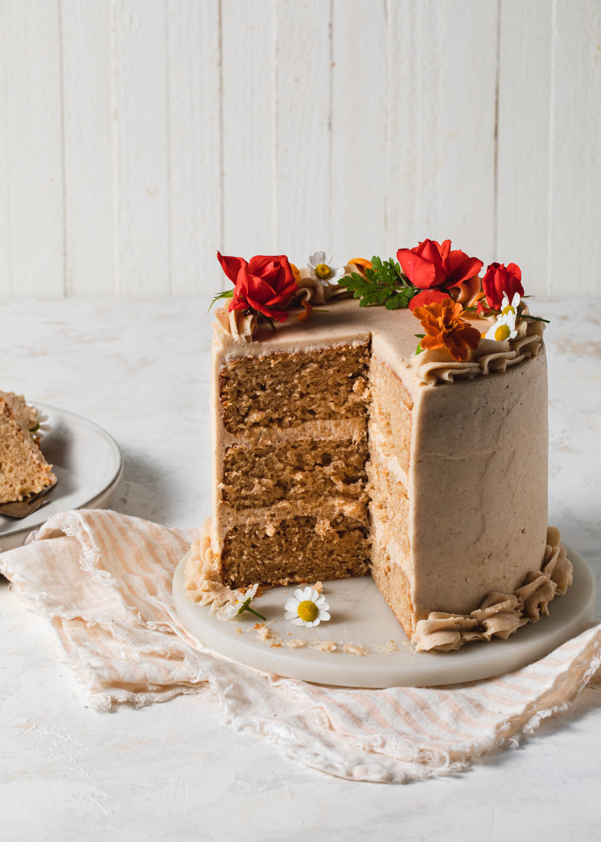 A sliced, three-layer pear cake with cinnamon buttercream decorated with fresh flowers