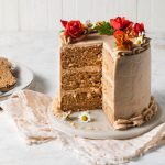 A sliced, three-layer pear cake with cinnamon buttercream decorated with fresh flowers