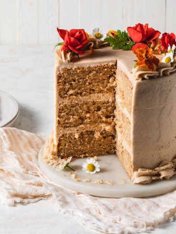 A sliced, three-layer pear cake with cinnamon buttercream decorated with fresh flowers