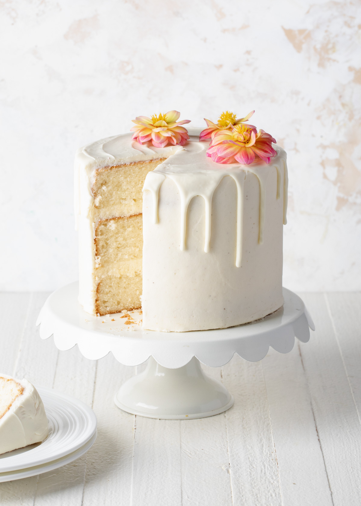 An all white chocolate drip cake with pink flowers on top.