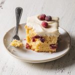 A slice of orange cranberry cake with vanilla frosting on a plate