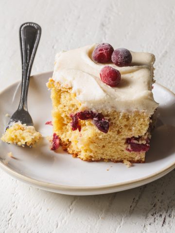 A slice of orange cranberry cake with vanilla frosting on a plate