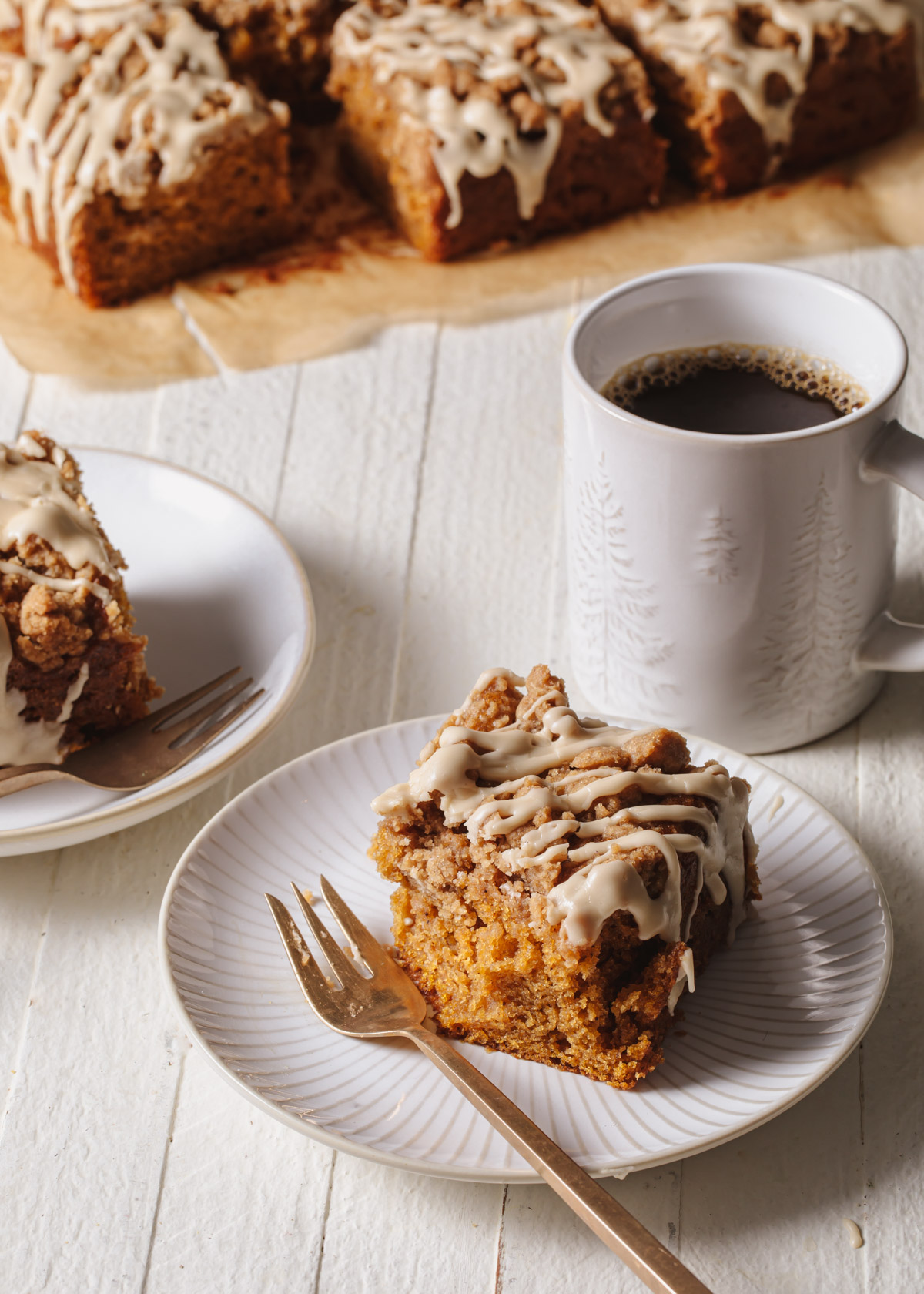 A square of pumpkin coffee cake on a plate with a mug of coffee