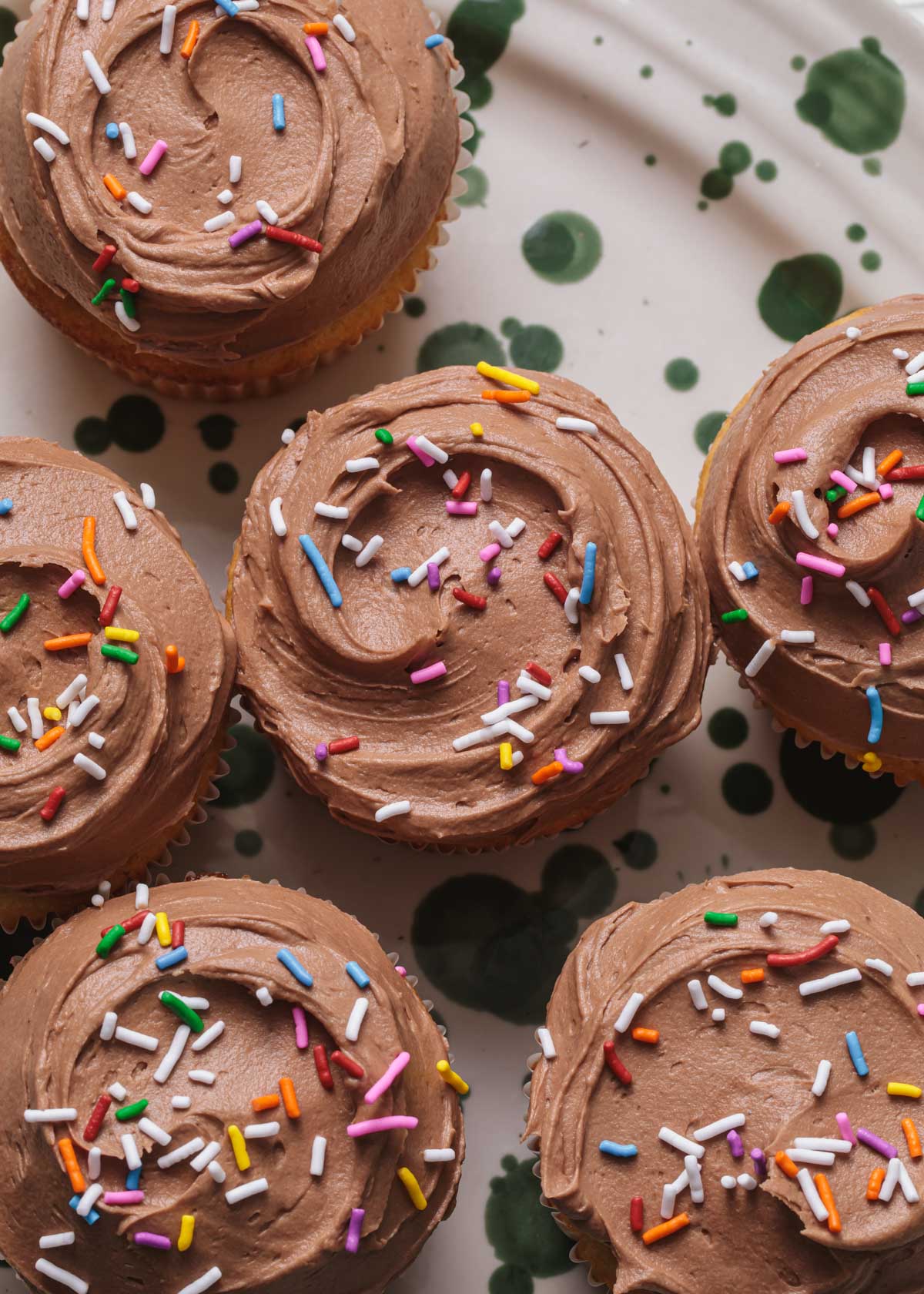The tops of cupcakes frosted with milk chocolate buttercream and sprinkles